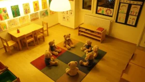 Scenariusz Dnia Pluszowego Misia w przedszkolu - grupka pluszowych misiów siedząca w kole na kolorowym dywanie w sali przedszkolnej